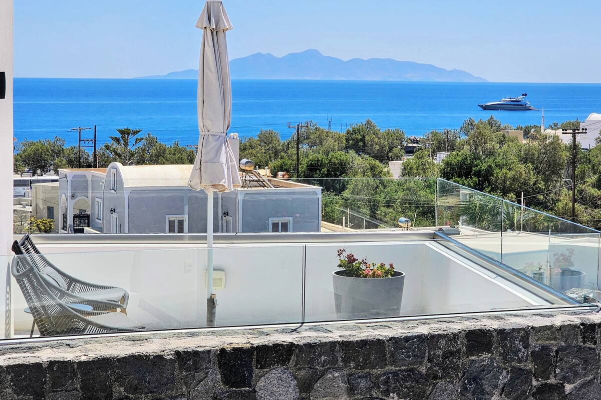 Eine Dachterrasse mit Blick auf das Meer, einem weißen Sonnenschirm und einem Blumentopf.