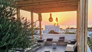 Terraza en la azotea con asientos, luces colgantes y vistas al atardecer sobre el mar.