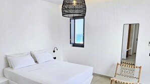 Un dormitorio moderno con una cama grande, una ventana pequeña, una lámpara de pared y una silla.