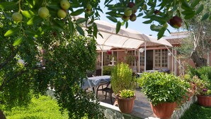 Eine Terrassenfläche mit Tisch, Stühlen und Topfpflanzen, sowie ein Gebäude mit einem Ziegeldach.