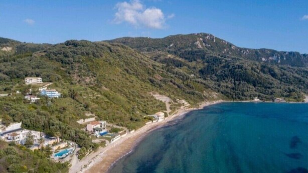 Eine Küstenlandschaft mit Strand, Berg und einem Gebäudekomplex mit mehreren Bauten.