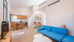 Ein modernes Wohnzimmer mit einem blauen Sofa, einem weißen Tisch und einem Fernseher auf einem Holzständer.