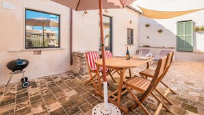 Eine Terrasse mit Tisch, Stühlen, einem Grill und einem großen Sonnenschirm.