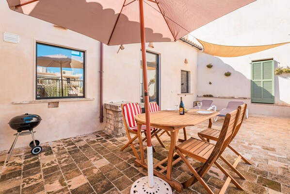 A patio with a table and chairs, a grill, and a large umbrella.