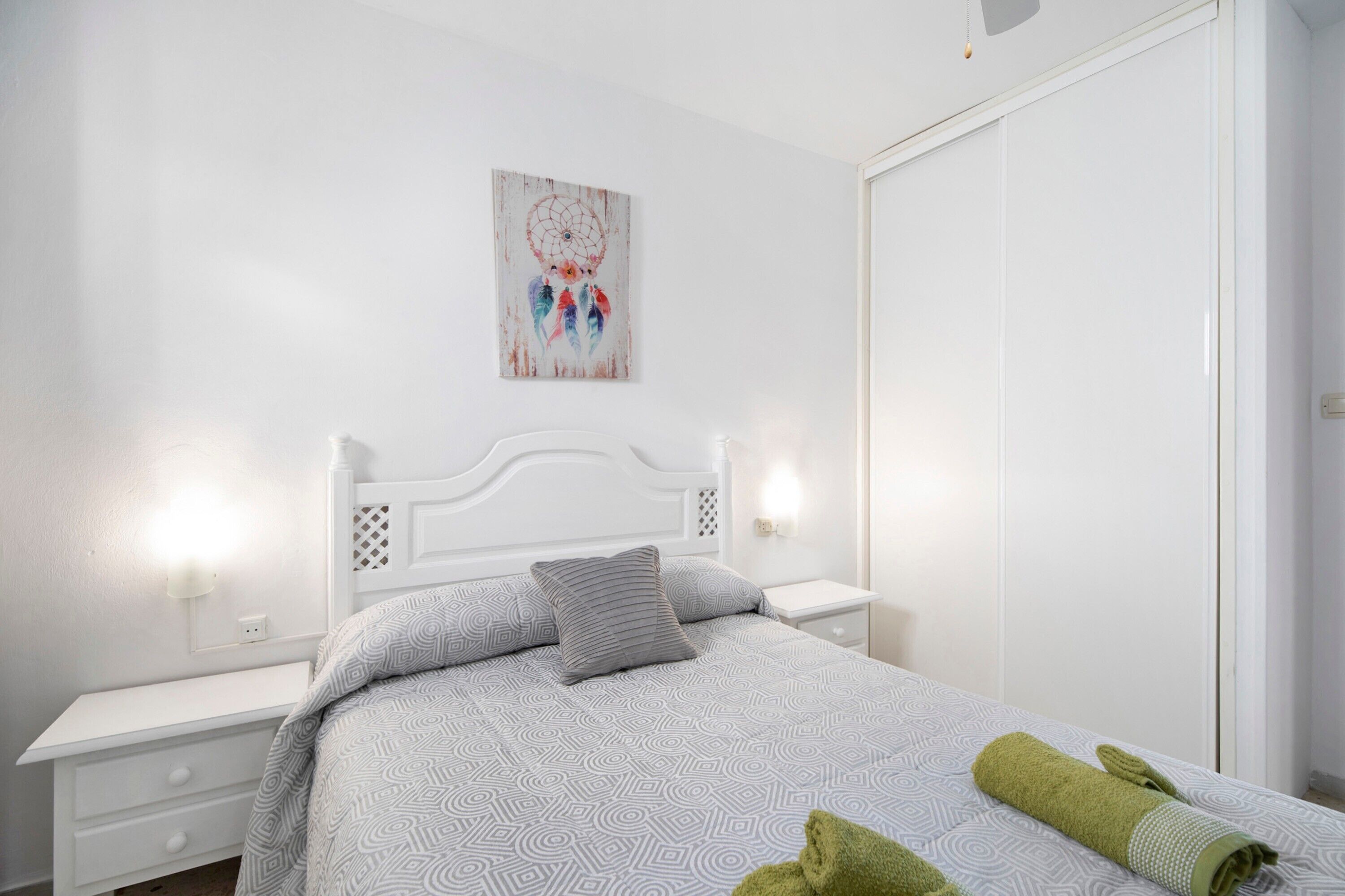 Een keurig opgemaakte slaapkamer met een bed, nachtkastjes en een aan de muur bevestigd kunstwerk.