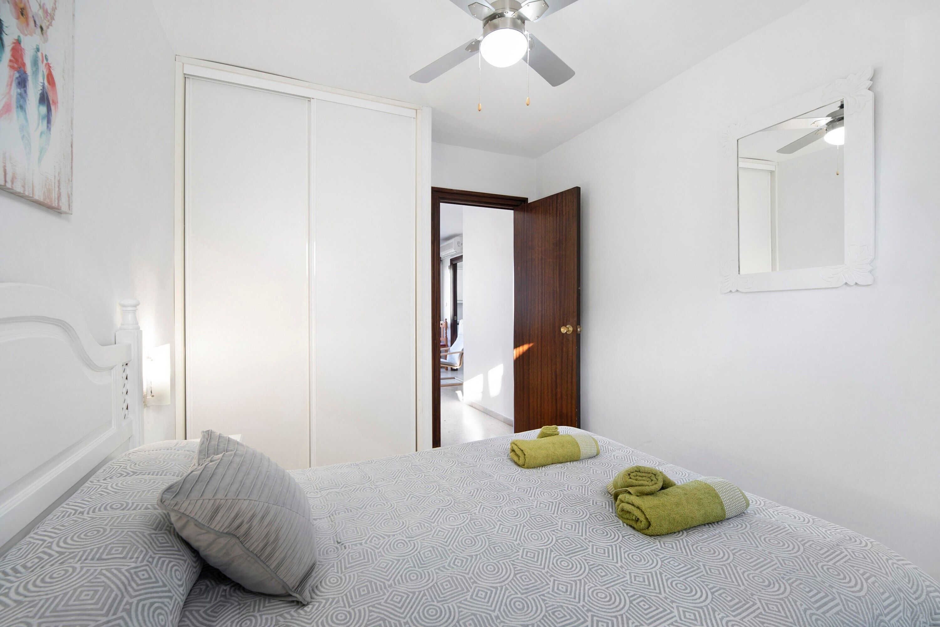 Een slaapkamer met een bed, een plafondventilator, een deur en een spiegel.