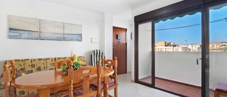 A dining area with a wooden table and chairs, a sofa, and a view of the city through a sliding glass door.