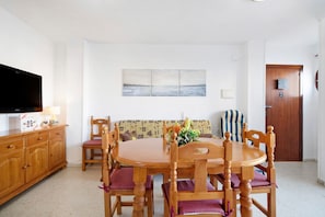 A dining area with a wooden table and chairs, a television on a cabinet, and a wall-mounted painting. - Apartment "Sol y mar" with Balcony & A/C (Sanlúcar de Barrameda)