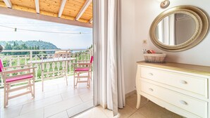 Ein Balkon mit Tisch und Stühlen, eine Kommode mit Schubladen, ein Spiegel und Blick auf Grünflächen und Hügel.