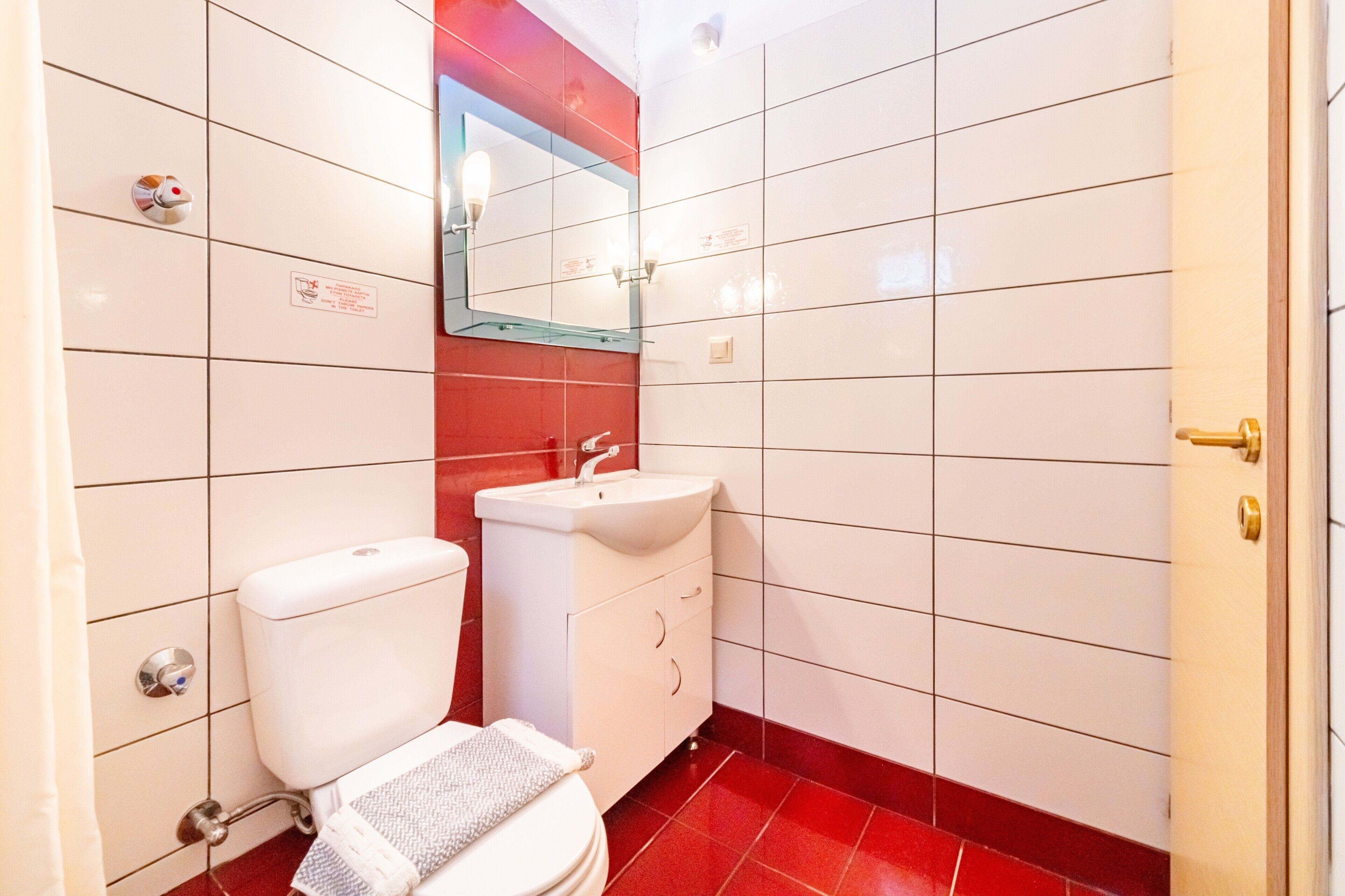 A bathroom with a toilet, sink, mirror, and red-tiled walls.