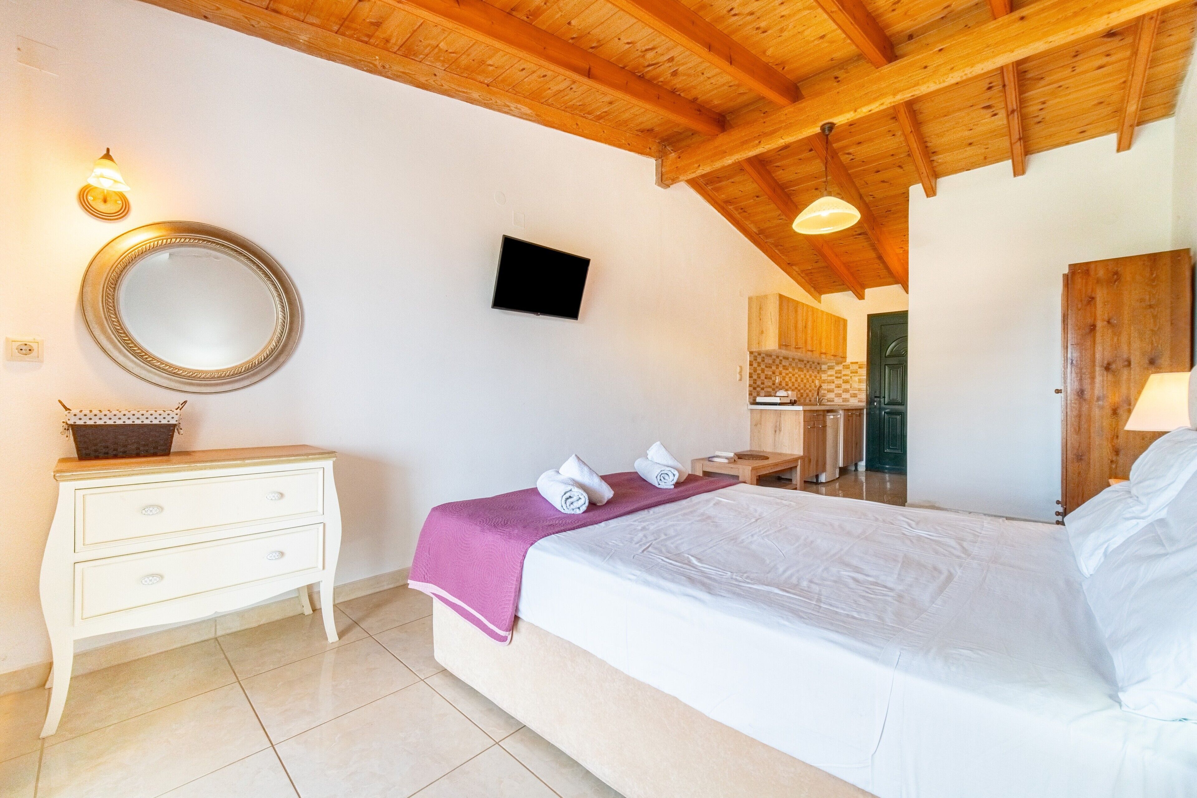 Une chambre à coucher avec un lit, une commode, un téléviseur et un plafond en bois.