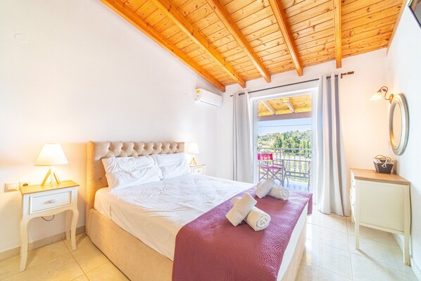 A bedroom with a wooden ceiling, a bed with white bedding, a nightstand with a lamp, and a view of a balcony.