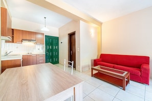 A modern kitchen with wooden cabinets, a dining table, and a red sofa in a living area.