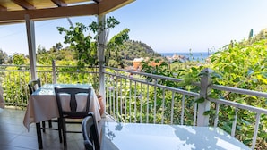 A covered balcony with a table and chairs, overlooking a scenic landscape with trees and a view of the sea. - Studio Apartment 'Arianna Superior Studio 19' with Shared Pool & Wi-Fi (Corfu)