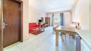 A living room with a red sofa, a wooden coffee table, a dining table with chairs, a TV, and a balcony with a view. - Studio Apartment 'Arianna Superior Studio 19' with Shared Pool & Wi-Fi (Corfu)