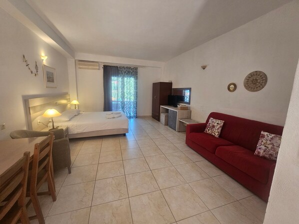 Quarto de hotel com cama, escrivaninha com cadeira, sofá vermelho e televisão.