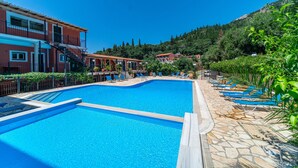 A swimming pool with lounge chairs, a stone deck, and buildings in the background. - Studio Apartment 'Arianna Superior Studio 18' with Shared Pool, Balcony & Wi-Fi (Corfu)