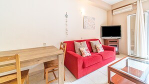 A living room with a red sofa, a wooden dining table, a TV, and a glass coffee table. - Studio Apartment 'Arianna Superior Studio 18' with Shared Pool, Balcony & Wi-Fi (Corfu)