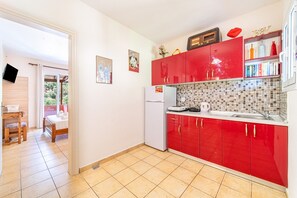 A compact kitchen with red cabinets, a tiled backsplash, and a small refrigerator.