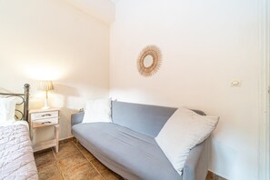 A bedroom with a bed, a bedside table with a lamp, a sofa, and a wall-mounted mirror.