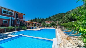Ein Swimmingpool mit Liegestühlen, einer Steinterrasse und Gebäuden im Hintergrund.