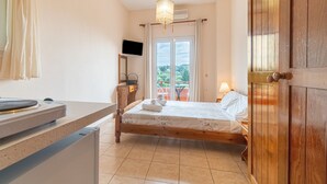 Ein Schlafzimmer mit einem Bett, einem Schreibtisch, einem Fernseher und einem Fenster mit Vorhängen.