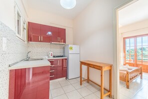 Eine kleine Küche mit roten Schränken, einem weißen Kühlschrank und einem Holztisch.