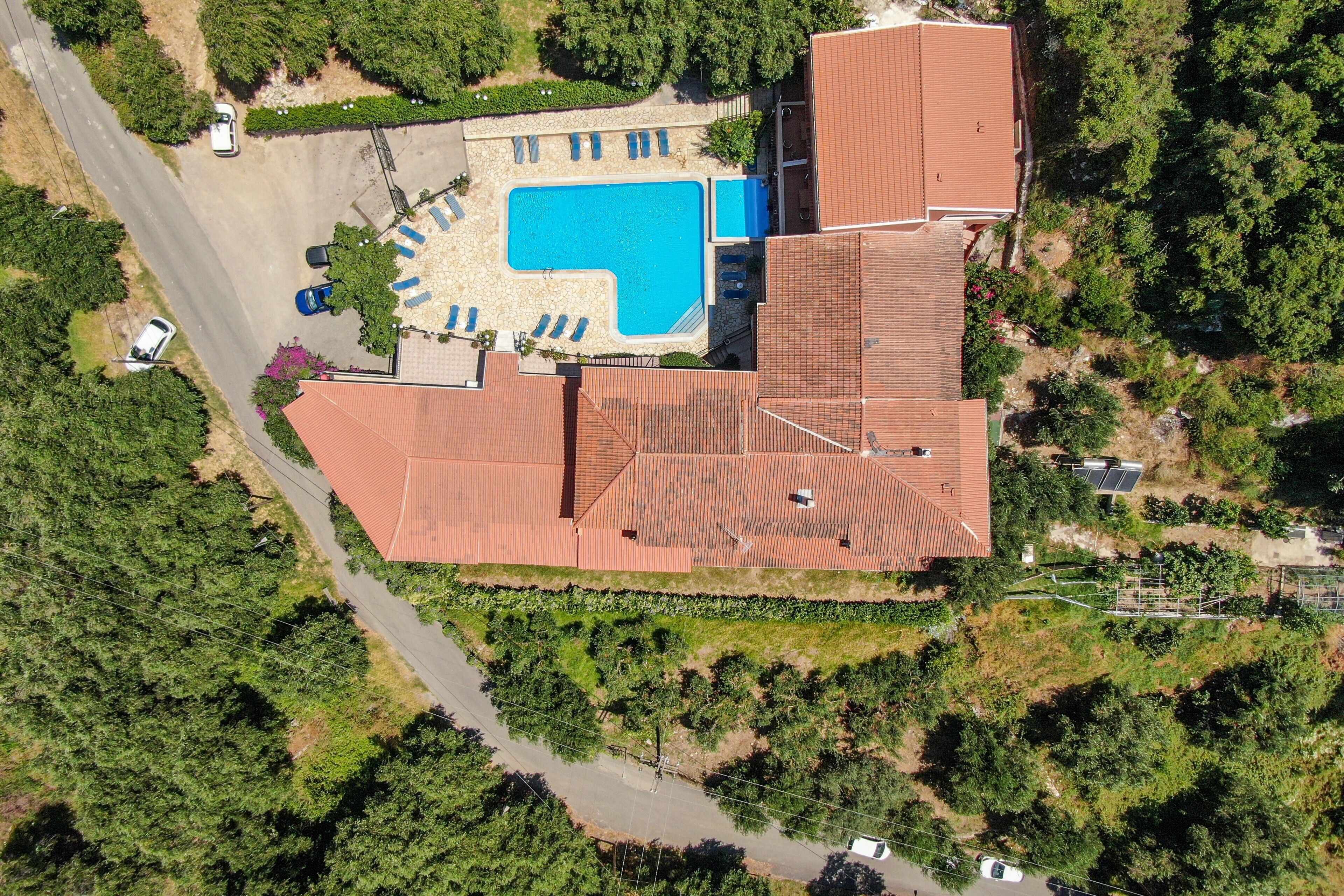 An aerial view of a property with a swimming pool, multiple buildings, and surrounding greenery.