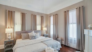 A bedroom with a large bed, two bedside tables with lamps, a bench, and a fireplace.