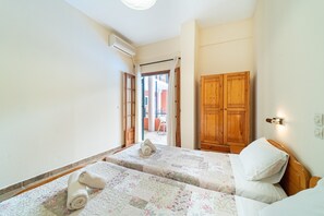 Een hotelkamer met twee bedden, een houten garderobe, een airconditioning en uitzicht door een open deur.