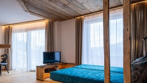 Een kamer met een bed, een televisie, een houten bankje en grote ramen met gordijnen.
