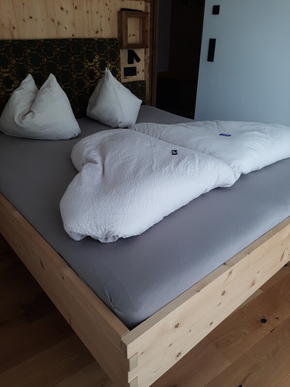 A wooden bed with a grey mattress, white pillows, and a wooden headboard with a decorative pattern.