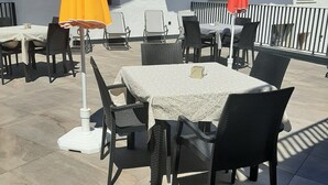 Een terras buiten met tafels, stoelen, parasols en een gebouw met een balkon.