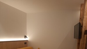 Een kamer met een gele bank, een flatscreen televisie bevestigd aan een houten wand, en een houten vloer.