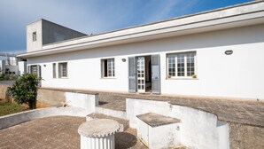 Ein weißes Gebäude mit mehreren Fenstern, einer Tür und einem kleinen Gartenbereich mit einem Betonpflanzkübel.
