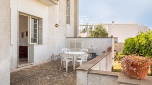 Eine Terrasse mit Tisch und Stühlen, einem Blumentopf und einem Gebäude mit Tür und Fenster.