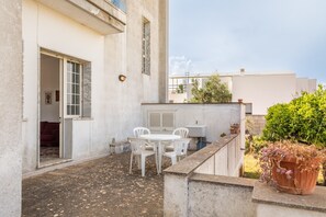 Une terrasse avec une table et des chaises, une plante en pot et un bâtiment doté d’une porte et d’une fenêtre.