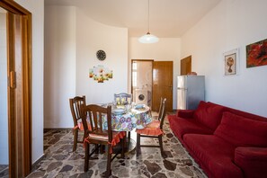 Un comedor con una mesa preparada para cuatro personas, rodeada de sillas, un sofá rojo, una lavadora y un refrigerador.