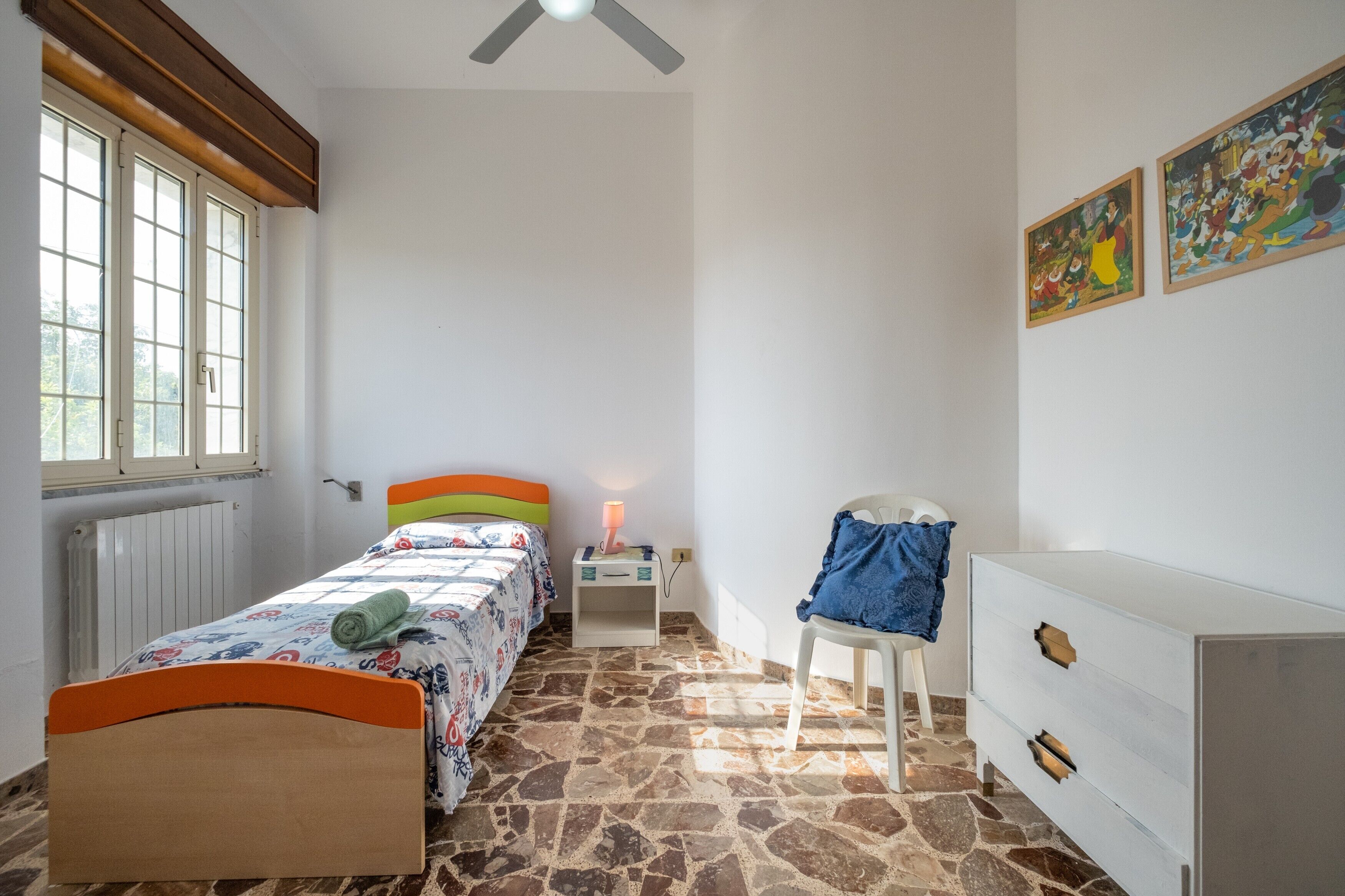 Un dormitorio con cama, una silla, cómoda, mesita de noche y ventana.