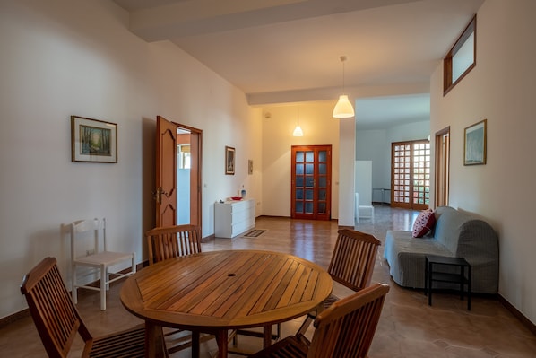 A dining area with a wooden table and chairs, a sofa, and a small table with a lamp.