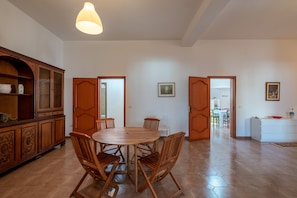 A dining area with a round wooden table and chairs, a cabinet with glass doors, and a hanging light fixture.