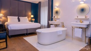 Una habitación de hotel moderna con una cama grande, una zona de estar separada, una bañera, un tocador con espejo y un estante pequeño con artículos de aseo.