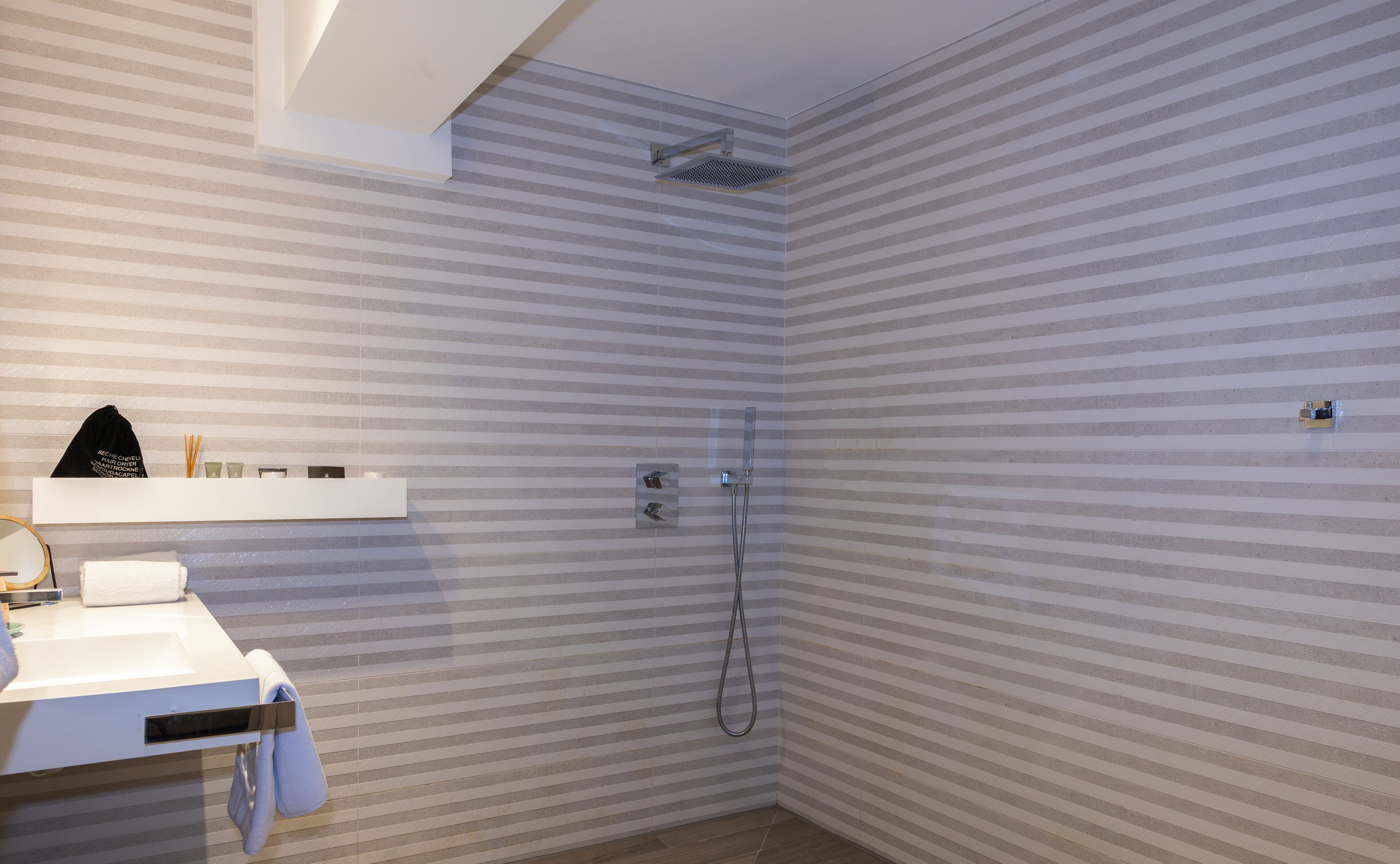 A bathroom with striped wallpaper, a shower, a sink, and a towel rack.