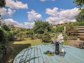 A round table with a bottle and a glass of wine, surrounded by greenery and a wooden fence. - Buzzards Breg (Builth Wells)