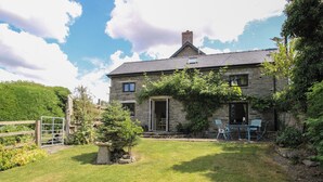 Une maison en pierre avec une cour verdoyante, une clôture en bois et une petite table de jardin.