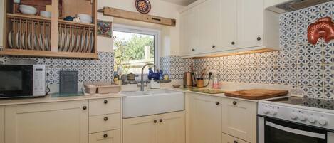 A kitchen with a microwave, stove, sink, and wooden utensil rack.