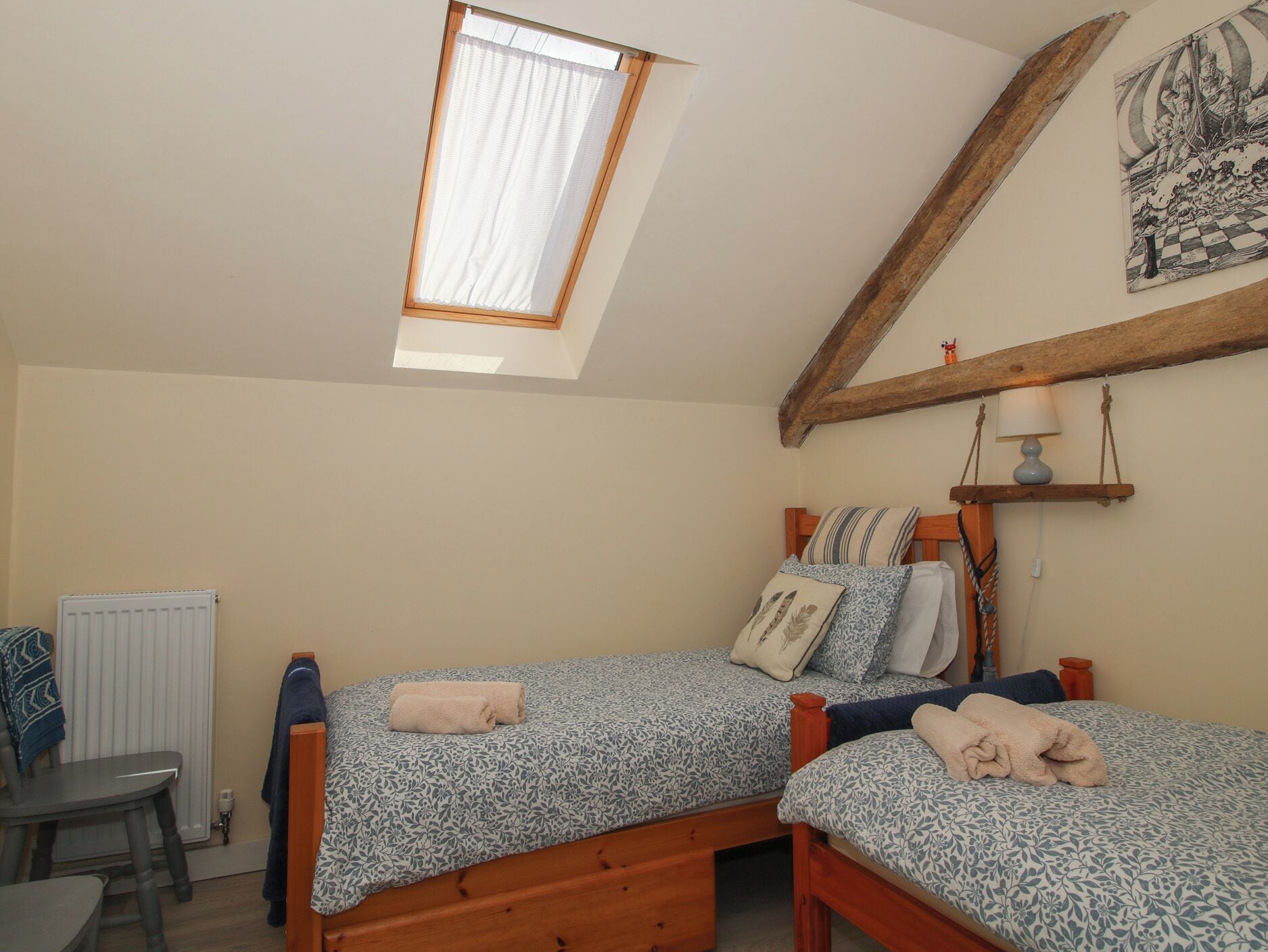 A bedroom with two beds, a window, a radiator, and a wooden ceiling beam.