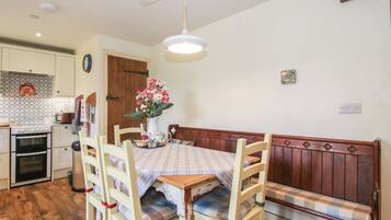 A dining area with a wooden table, chairs, a bench, a flower vase, and a kitchen in the background.