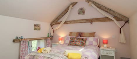 A bedroom with a sloped ceiling, a bed with a colorful quilt, two bedside lamps, and a window with curtains.