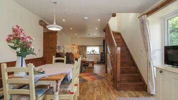 A cozy interior with a wooden staircase, a dining area with a table set for two, and a television on a stand.